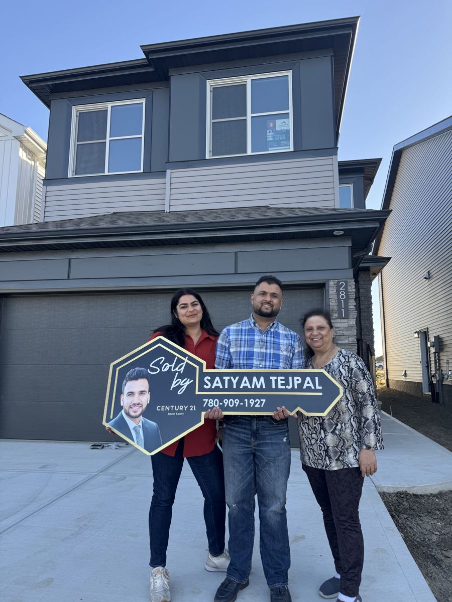 Three new homeowners holding a Sold key sign in front of a new two-storey home