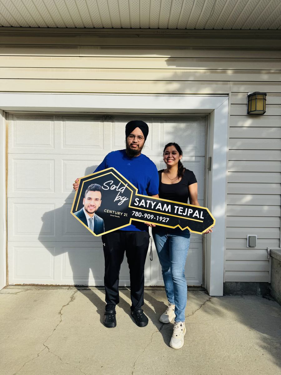 A couple holding a Sold key sign in front of their garage