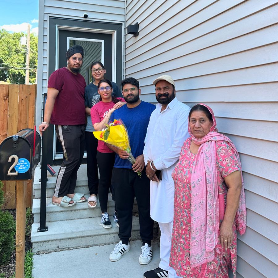 A family of six on the front steps of their new home, one holding a bouquet of flowers